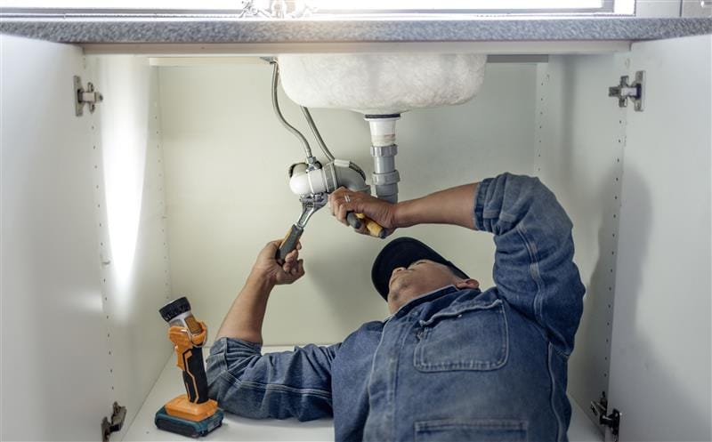Plumber repairing pipes beneath a bathroom sink in Ladera Ranch
